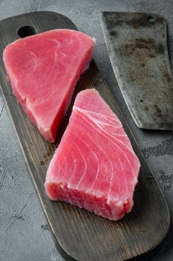 Çiğ ton balığı parçaları, ahşap kesim tahtasının üzerinde, ve eski kasap satır bıçağı, gri taş arka planda