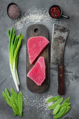 Çiğ ton balığı filetosu. Yeşil bezelyeli deniz ürünleri, susam ve malzeme seti ahşap kesme tahtasına, ve eski kasap satır bıçağı, gri taş arka plan, üst düz yatıyordu