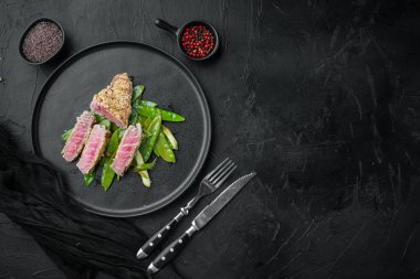 Ton balıklı susamlı meze. Bahar soğanı ve bezelyeli. Tabakta, siyah taş zemin üzerinde.