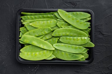 Şekerli bezelyeler, taze olgun bebek kabukları, plastik kabın içinde, siyah taş zemin üzerinde, üst manzara düz yatıyordu.