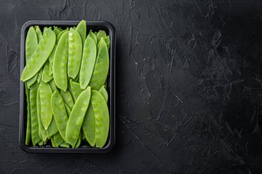 Sağlıklı bezelye seti, plastik kabın içinde, siyah taş zemin üzerinde, üst görünüm düz, metin için telif alanı ve boşluk ile