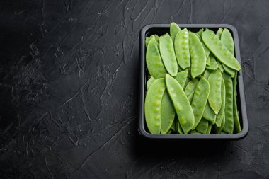 Organik Yeşil Şeker Bezelyeleri Plastik kabın içinde, siyah taş zemin üzerinde, metin için metin alanı ve boşluğu ile hazır.