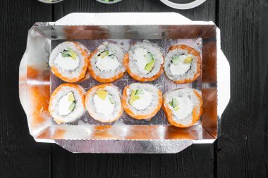 Farklı suşi çeşitleri ve rulo fro, somon ve ton balığı teslimat konsepti seti, siyah ahşap masa arka planı, üst görünüm düz yatıyordu