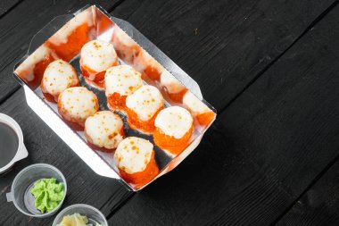 Lezzetli suşi tek kullanımlık kutularda, siyah ahşap masa zemininde, metin için metin alanı ve boşluğu ile yuvarlanıyor.