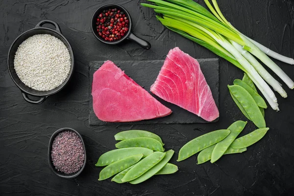 Çiğ ton balığının malzemeleri yeşil bezelye, susam ve bitkiler, taş tahtada, siyah taş zemin üzerinde, üst görünüm düz
