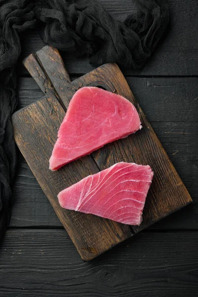 Taze çiğ ton balıklı biftek seti, ahşap kesim tahtası, siyah ahşap arka plan, üst manzara düz.