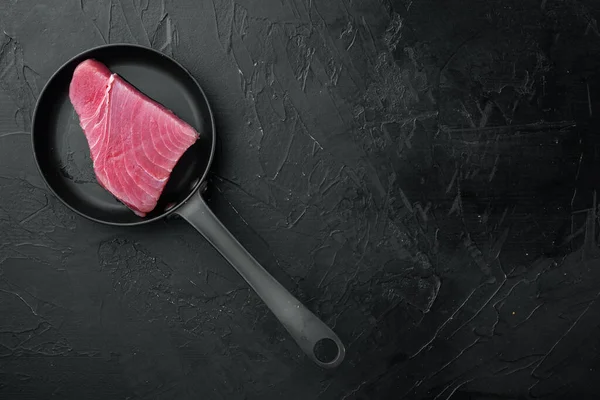 Çiğ ton balığı setinin parçaları, kızgın demir tavada, siyah taş zemin üzerinde, telif alanı ve metin için yeri olan üst görünüm düz yerde.