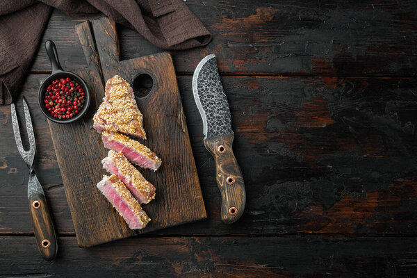 Sliced grilled Tuna steak in sesame and soy sauce set, on wooden serving board, on old dark  wooden table background, top view flat lay , with copyspace  and space for text