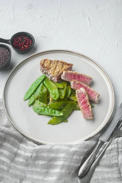 Ton balıklı ızgara biftek, taze soğan ve bezelye, tabakta, beyaz taş zemin üzerinde.