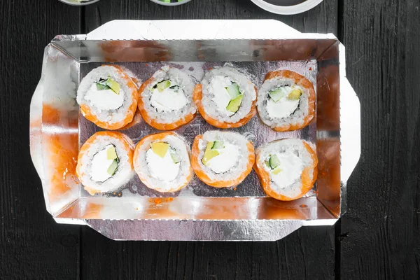 Farklı suşi çeşitleri ve rulo fro, somon ve ton balığı teslimat konsepti seti, siyah ahşap masa arka planı, üst görünüm düz yatıyordu