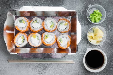 Lezzetli suşi tek kullanımlık kutularda yuvarlanıyor, gri taş arka planda, en üstteki düz manzarada.