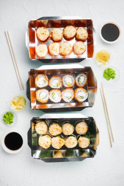 Suşi servis konteynırında yuvarlanıyor, beyaz taş zemin üzerinde, üst manzara düz.