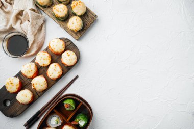 Somon, yengeç, salatalık, avokado, uçan balık yumurtası ve baharat soslu fırınlanmış suşi maki ruloları, beyaz taş zemin üzerinde, üst görünüm düz, metin için metin alanı ve yeri var.