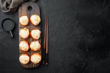 Somon, yengeç, salatalık, avokado, uçan balık yumurtası ve baharat soslu fırınlanmış suşi maki ruloları, siyah taş zemin üzerinde, üst manzara düz, metin için metin alanı ve yeri var.