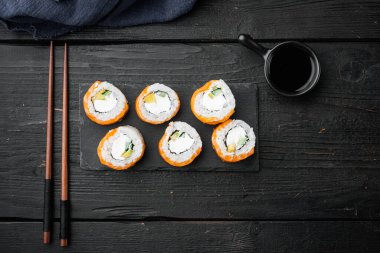 Suşi rulo somon ve ton balığının yemek çubukları seti, siyah ahşap masa arkaplanı, üst görünüm düz, metin için telif alanı ve boşluk