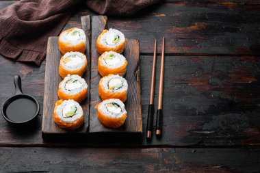 Suşi rulosu, Philadelphia somonlu, füme yılan balığı, avokado, krem peynir seti, eski siyah ahşap masa arka planında, metin için yer ve mekan.