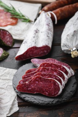 Kurutulmuş sucuk, fuet ve diğer sosisler eski ahşap masadaki otlarla dilimlenmiş..