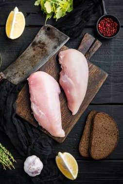 Çiğ tavuk filetosu, içinde kasap bıçağı ve siyah ahşap masa, üst manzara.