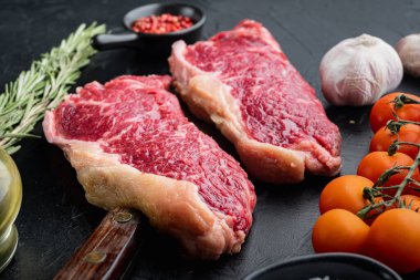 Strip fileto biftek, çiğ mermer et, siyah arka planda.