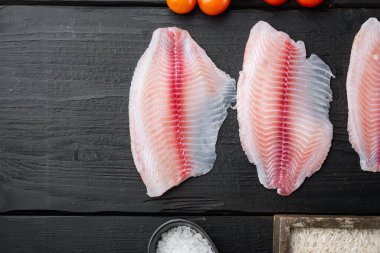 Çiğ beyaz tilapia balığı, basmati pilavı ve kiraz domatesleri ile siyah ahşap masa üzerinde, metin için fotokopi alanı ile üst görünüm