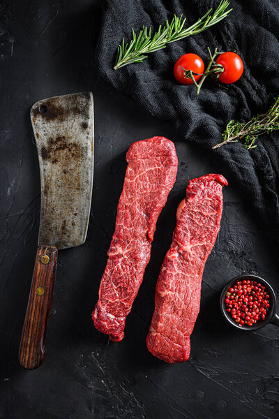 Raw marbled beef steak near butcher knife with pink pepper and rosemary. Black background. Top view.