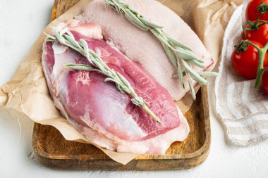 Ördek göğsü çiğ et seti, bitkiler ve malzemelerle, ahşap tepside, beyaz taş arka planda.