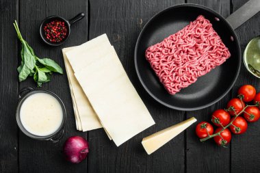 Lazanya pişirme konsepti. Malzemeler, lazanya çarşafları, fesleğen, kiraz domatesleri, parmesan, sarımsak, biber seti, siyah ahşap masa arka planı, üst görünüm, düz yatış.