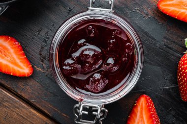 Doğal çilek reçeli kavanozu, eski koyu ahşap masa zemininde, üst manzara düz.