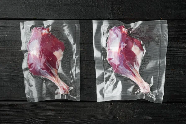 Raw duck leg meat in seal bag for sous vide cooking set, on black wooden table background, top view flat lay
