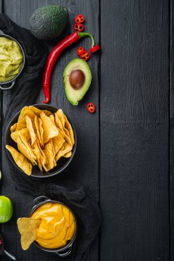 Siyah ahşap zemin üzerinde peynir ve guacamole soslu Meksika cipsi cipsi, üst görünüm veya düz metin alanı ile yatıyordu