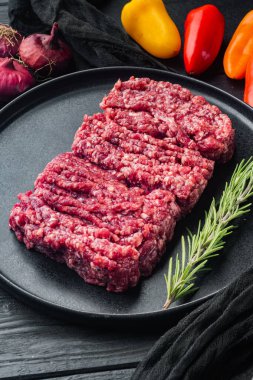Kıymalı biftek, siyah ahşap masa arkasında.