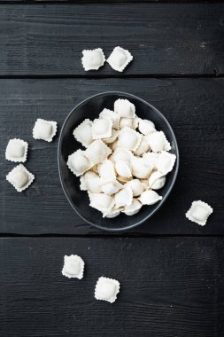 Donmuş tortellini ve Ravioli siyah kasede, tahta masa arkasında, üst manzara düz yatıyordu.