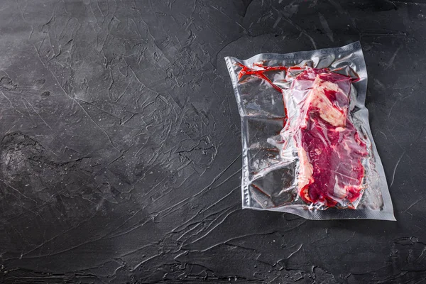 Vacuum packed organic beef  chuck roll steak for sous vide cooking  on black textured background, side view space for text
