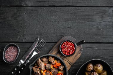 Sığır eti yahnisi servis edilir, dökme demir tavada, siyah ahşap zemin üzerinde, üst görünüm düz, metin için kopyalama alanı ile