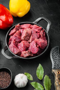 Gulaş pişirme seti için hazırlanmış sığır güveci. Tatlı dolma biberli, dökme demir tavada, siyah taş arka planda.