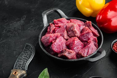 Taze çiğ et küpleri, tatlı dolma biberli, dökme demir tavada, siyah taştan arka planda.