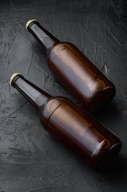 Cam şişelerde taze bira seti, siyah taş arka planda.