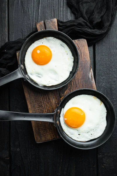 Scrambled eggs in frying pan with pork lard, bread and green feather in cast iron frying pan, on black wooden table background, top view flat lay