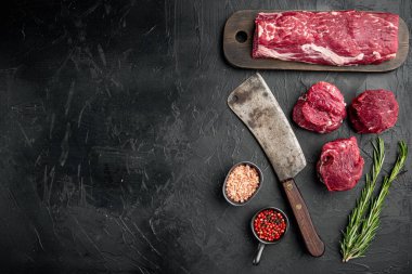 Taze Ham Biftek Mignon tüm set, eski kasap bıçağı ile, siyah taş arka planda, üst görünüm düz, metin için kopyalama alanı ile