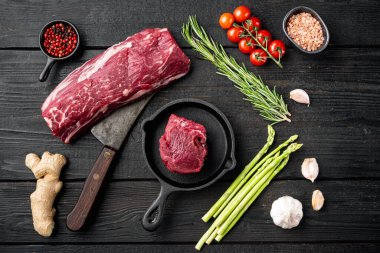 Çiğ biftek fileto fileto fileto seti, dökme demir kızartma tavasında, siyah ahşap masa arka planında, düz manzaralı