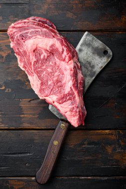 Pirzola eti çiğ et, eski kasap bıçağı ile kesilmiş, eski siyah ahşap masa arka planı, üst görünüm düz yatıyordu