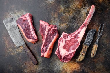 Çiğ Kara Angus Biftek seti, Tomahawk, kemik ya da biftek ve sopa biftek çeşitleri, eski kasap satırı bıçağı ile, eski siyah kırsal arka plan, üst düz yatıyordu