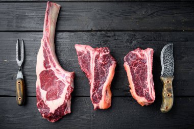 Çiğ Kara Angus Birincil Kuru Biftek seti, Tomahawk, kemik ya da biftek ve kulüp bifteği çeşitleri, siyah ahşap masa arka planında, üst görünüm düz yatıyordu