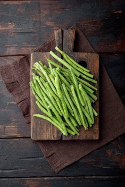 Yeşil çalı fasulyesi seti, ahşap kesim tahtası üzerinde, eski koyu ahşap masa arka planı, üst görünüm düz yatıyordu