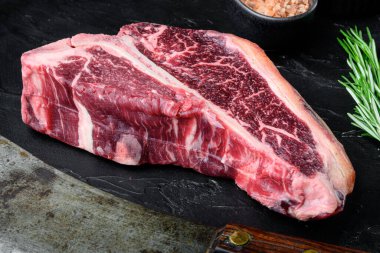 Çiğ et, baharatlı biftek, sarımsak ve biberiye seti, siyah taş arka planda.