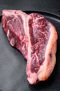 Kurumuş Raw T-bone ya da bifteği mermer kaplı, tabakta, siyah ahşap masa arkasında.