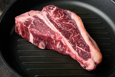 Kurumuş yıllanmış kemik bilyeli biftek seti, kızarmış demir tavada, eski siyah kırsal arka planda.