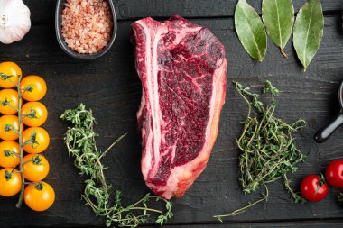 Çiğ biftek. Siyah angus eti seti, kulüp bifteği kesimi, siyah ahşap arka planda, üst manzara düz.