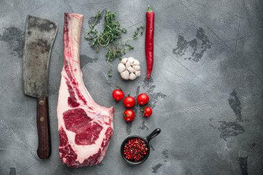 Tomahawk çiğ biftek ve baharatlar seti, ve eski kasap satır bıçağı, baharat ve otlarla, gri taş arka planda, üst görünüm düz metin için yer