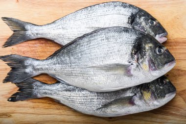 Çiğ dorada ya da doğrama tahtasına beyaz desenli arka plan görünümünde pişirilmemiş mangalda pişirilmemiş otlar yerleştirilmiş çipura balığı.